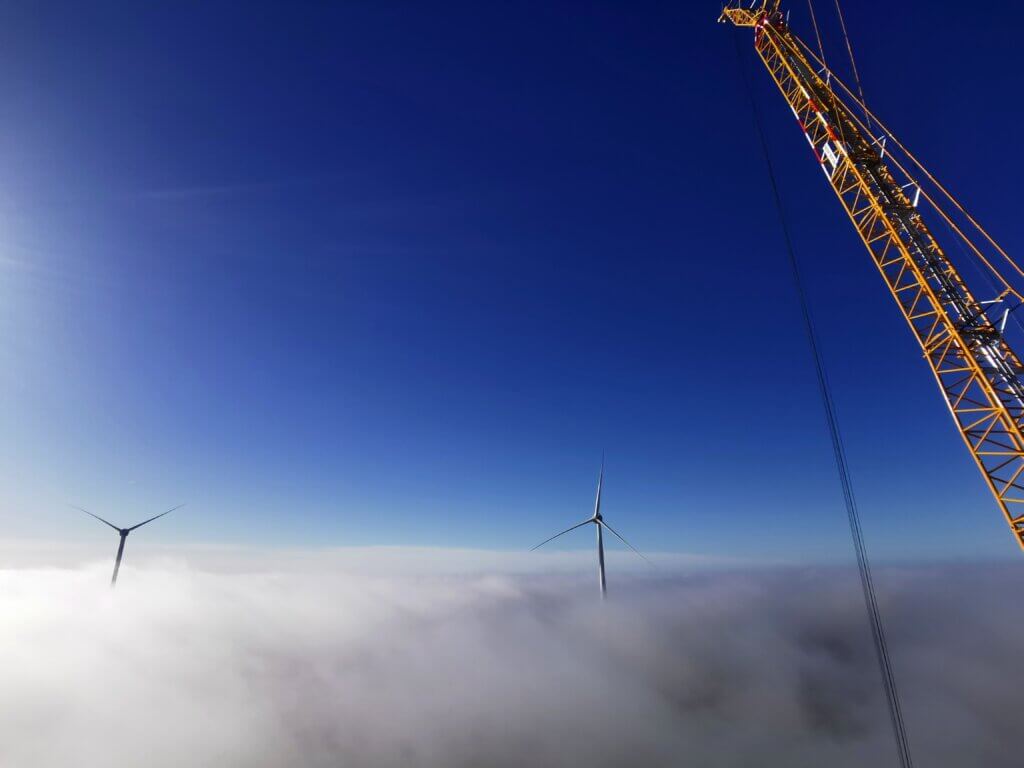 Image from the top of a wind turbine tower showing the view of the turbine blades above the clouds