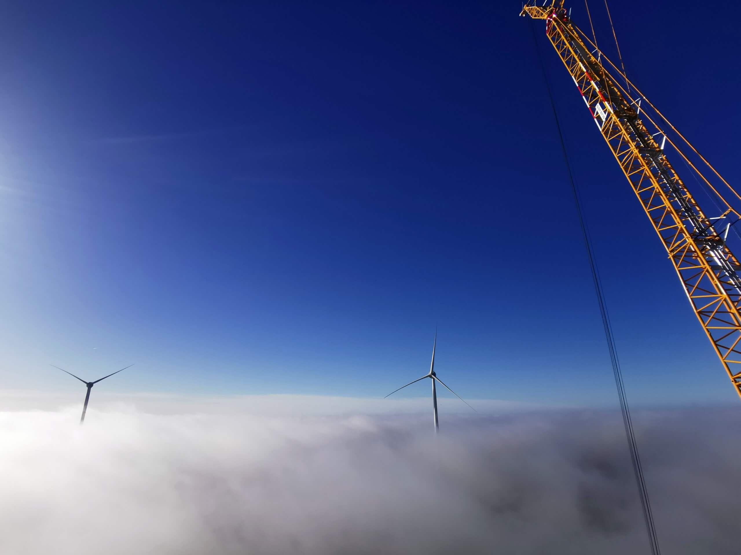 Image from the top of a wind turbine tower showing the view of the turbine blades above the clouds
